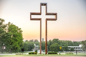 A bronze sculpture of an empty cross with a sunset in the background.